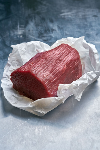 Beef Eye of Round beef perfect for Sunday roast,  on white paper against a textured gray background