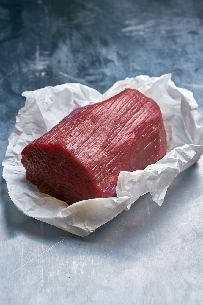 Beef Eye of Round beef perfect for Sunday roast,  on white paper against a textured gray background