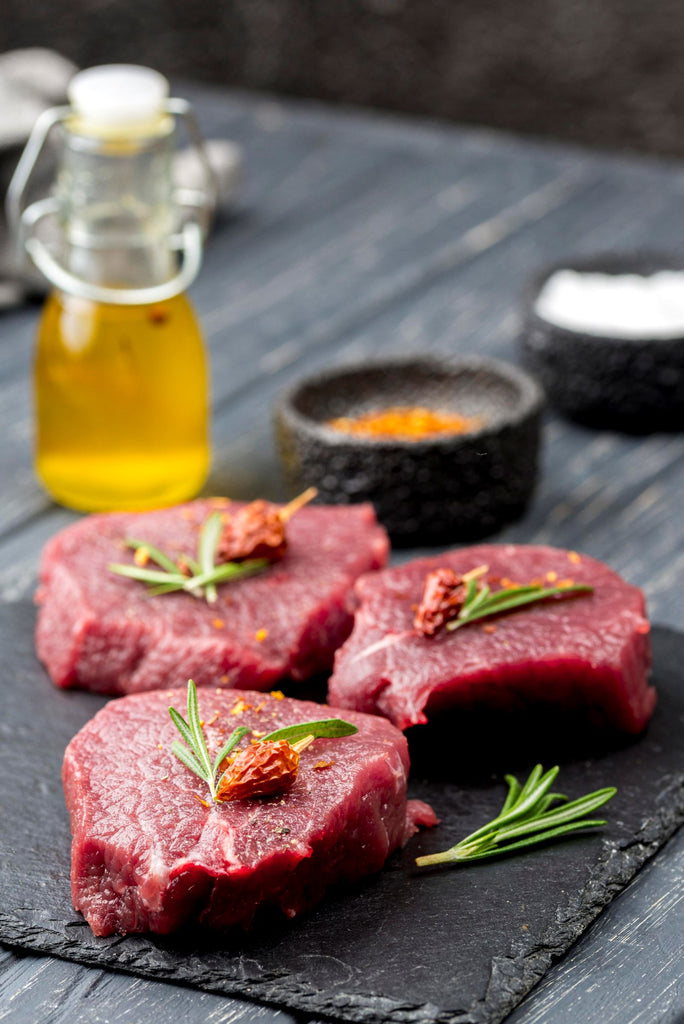 Raw Centre Cut Beef Fillet Steaks, hand-cut from 100% localised Irish Beef, ready to cook with seasonings on a dark surface