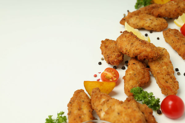 Cooked Southern Fried Chicken Goujons served with lemon wedges, cherry tomatoes, and fresh parsley on a white background.