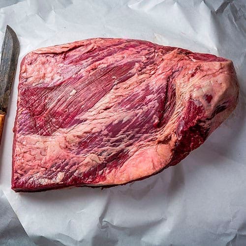 Herterich's Beef Brisket joint on white butcher paper with a knife, ready for slow-cooking or smoking.