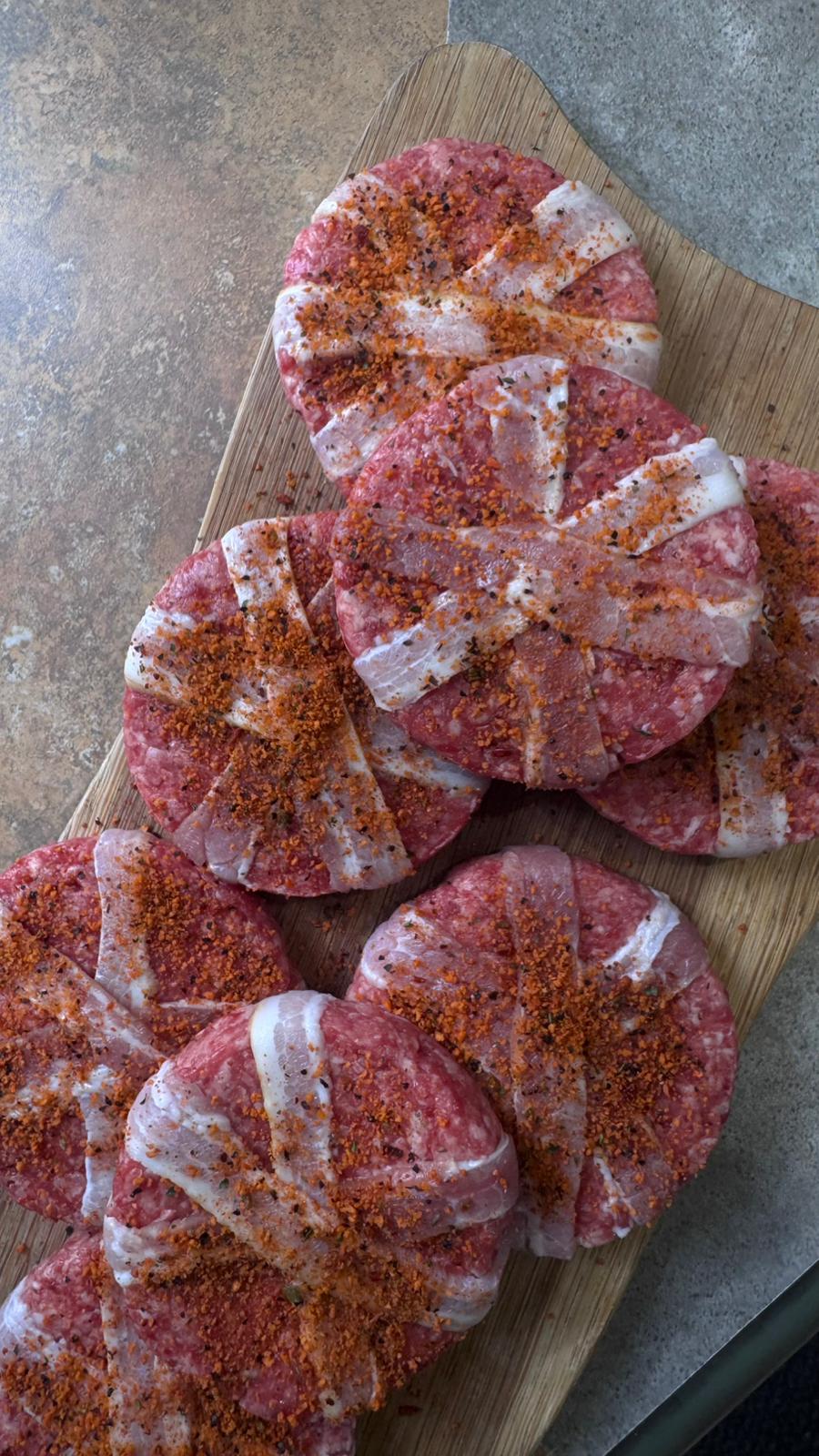 Herterich Artisan Meats raw smokey bacon wrapped beef burger patties seasoned on wooden board