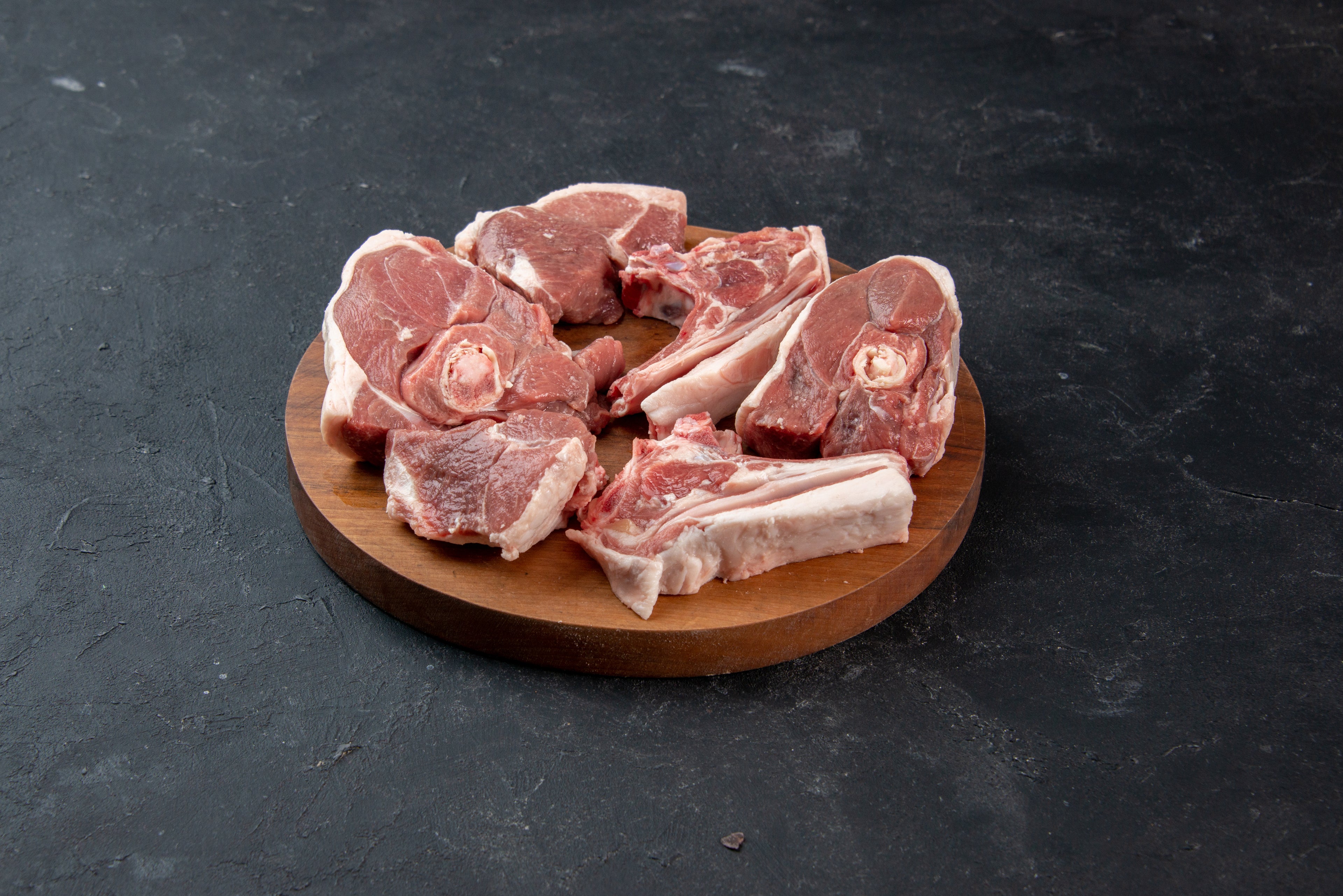 Fresh raw Irish shoulder lamb chops on a round wooden board from Herterich Artisan Meats
