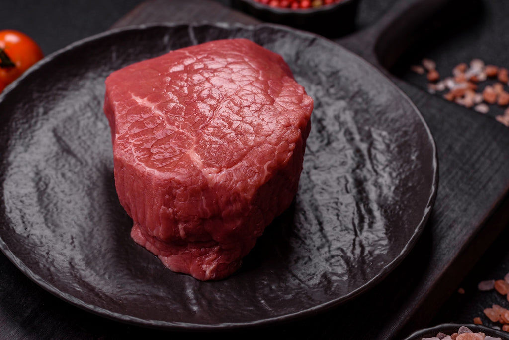 Raw Round Roast Beef on a dark plate with spices in the background