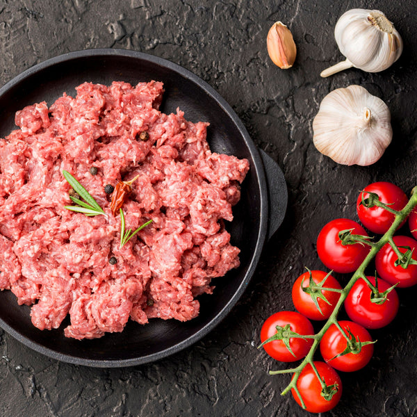 Ground sausage meat in a black pan with garlic, tomatoes, and herbs on a dark surface
