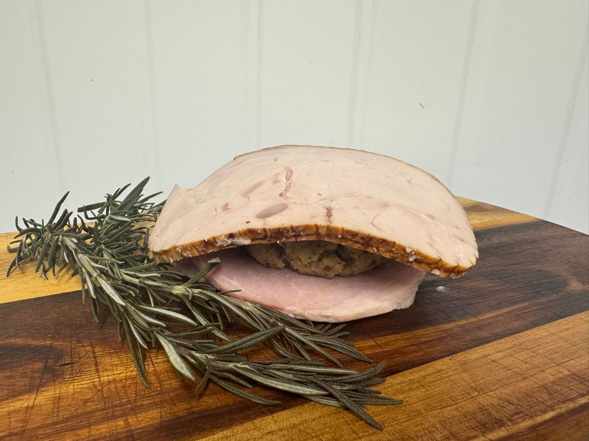 Individual 390g portion of sliced cooked turkey and ham with stuffing, served on a wooden board with fresh rosemary.