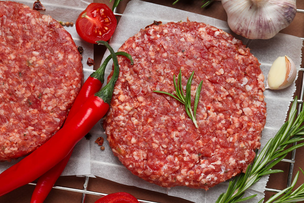 Wagyu Beef Burgers surrounded by chilies, garlic and rosemary