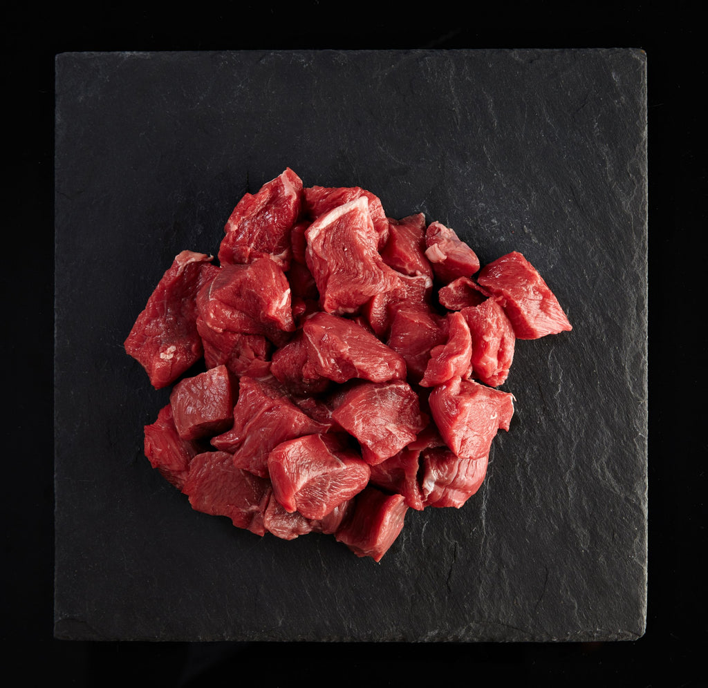 Raw diced beef chunks on a black slate surface