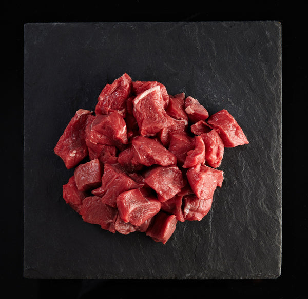 Raw diced beef chunks on a black slate surface