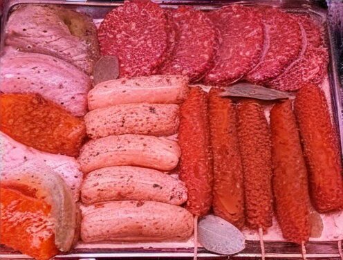 Assortment of raw meats in a butcher's display, including burgers, kebabs, and sausages, representing a BBQ special pack.