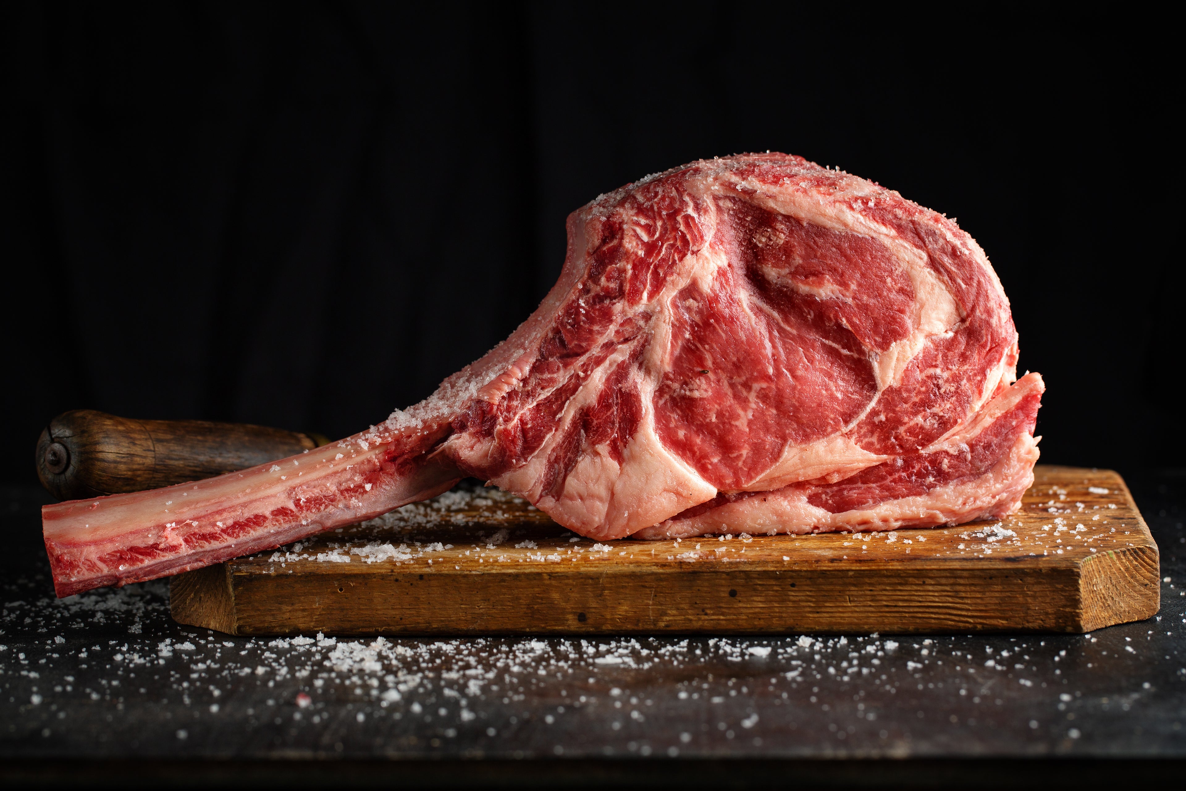 Premium dry aged Irish Tomahawk steak with sea salt on a wooden board from Herterich Artisan Meats