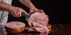 Person slicing a ham on a wooden board with a dark background