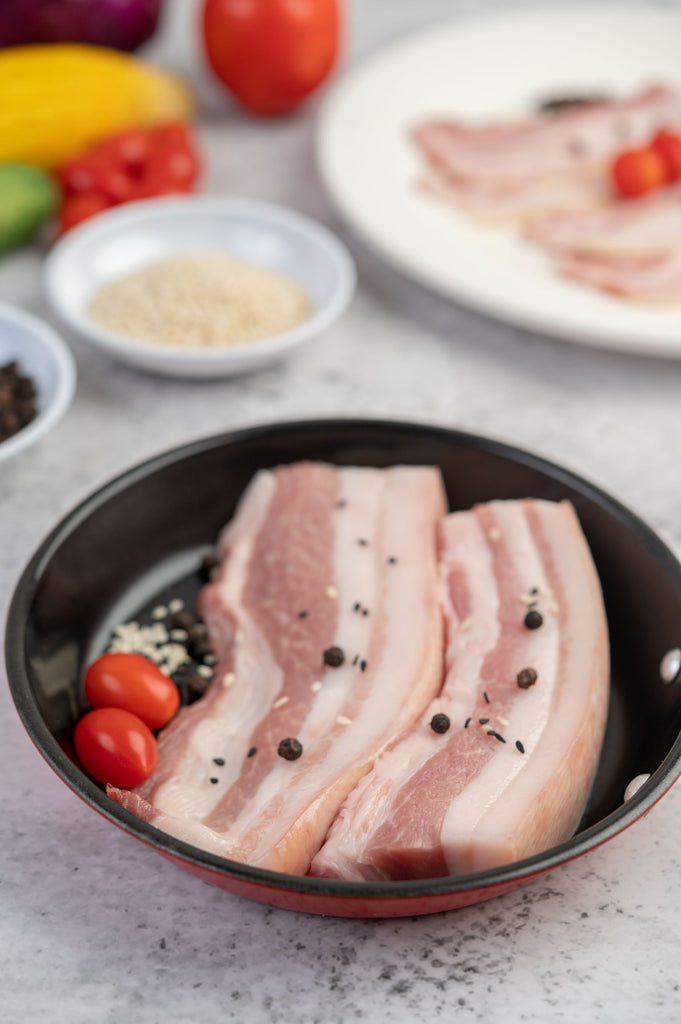 Herterich's Raw boneless Pork Belly Chops in a pan with seasonings and vegetables on a table
