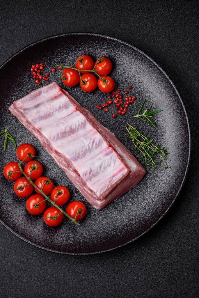 Herterich's Raw Pork Belly Joint with cherry tomatoes and herbs on a black plate
