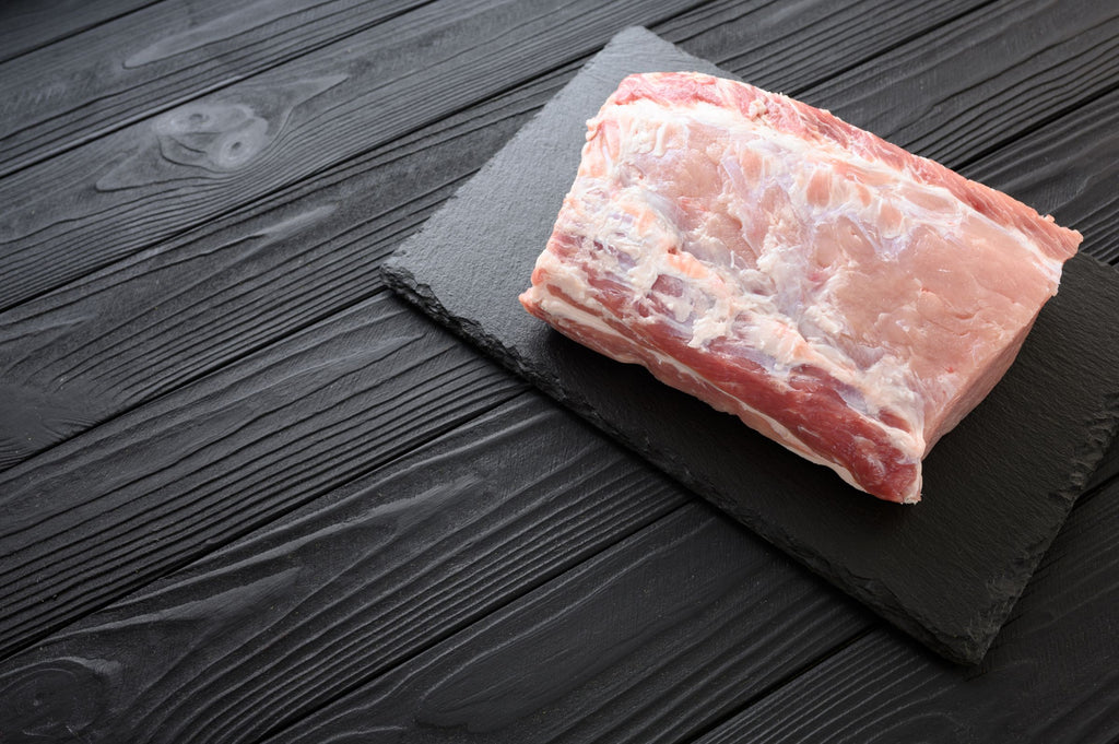 Raw Pork Loin Roast on a black slate board with a dark wooden background