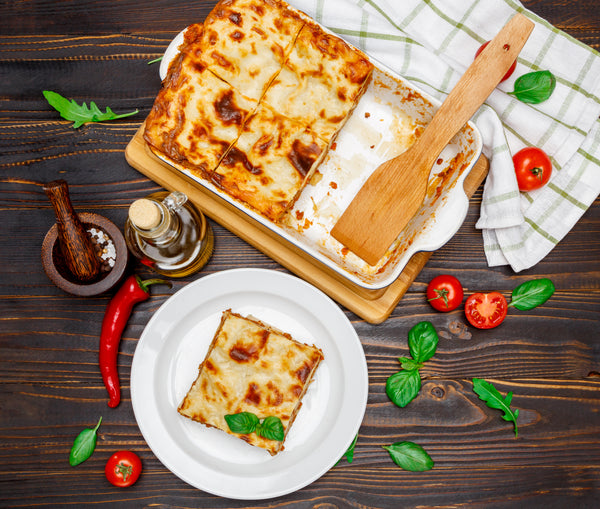 Baked Lasagna Family Tray Dinner with one slice served on a white plate, on a rustic wooden background.