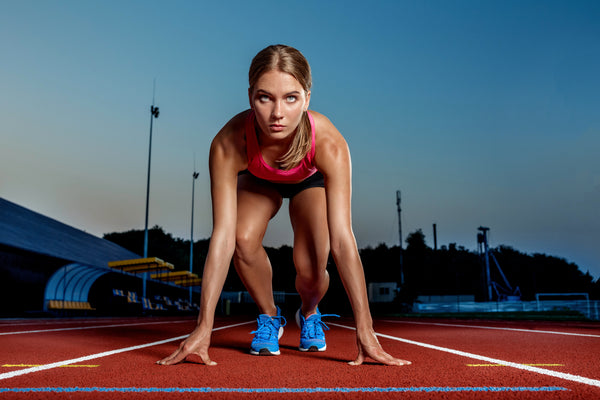 Female athlete in a starting block pose on a running track, symbolizing strength, performance, and fitness for a protein meat pack.