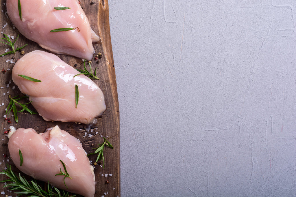 Raw chicken breasts with rosemary on a wooden board against a light gray background