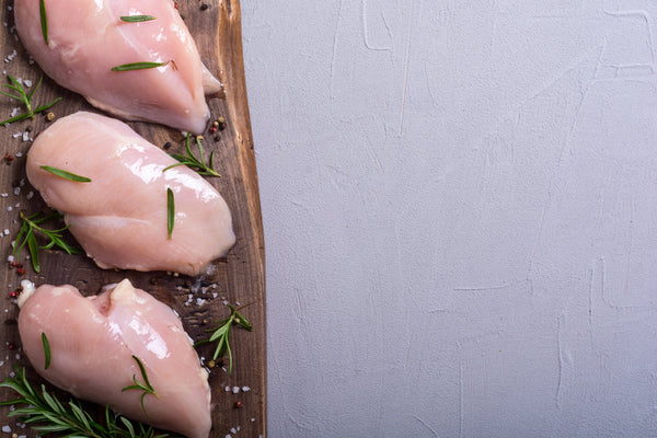 Raw chicken breasts with rosemary on a wooden board against a light gray background