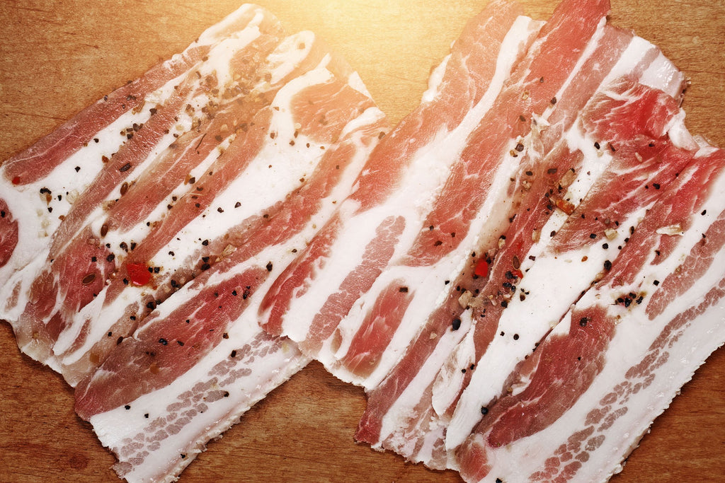 Raw smoked bacon strips with pepper on a wooden surface