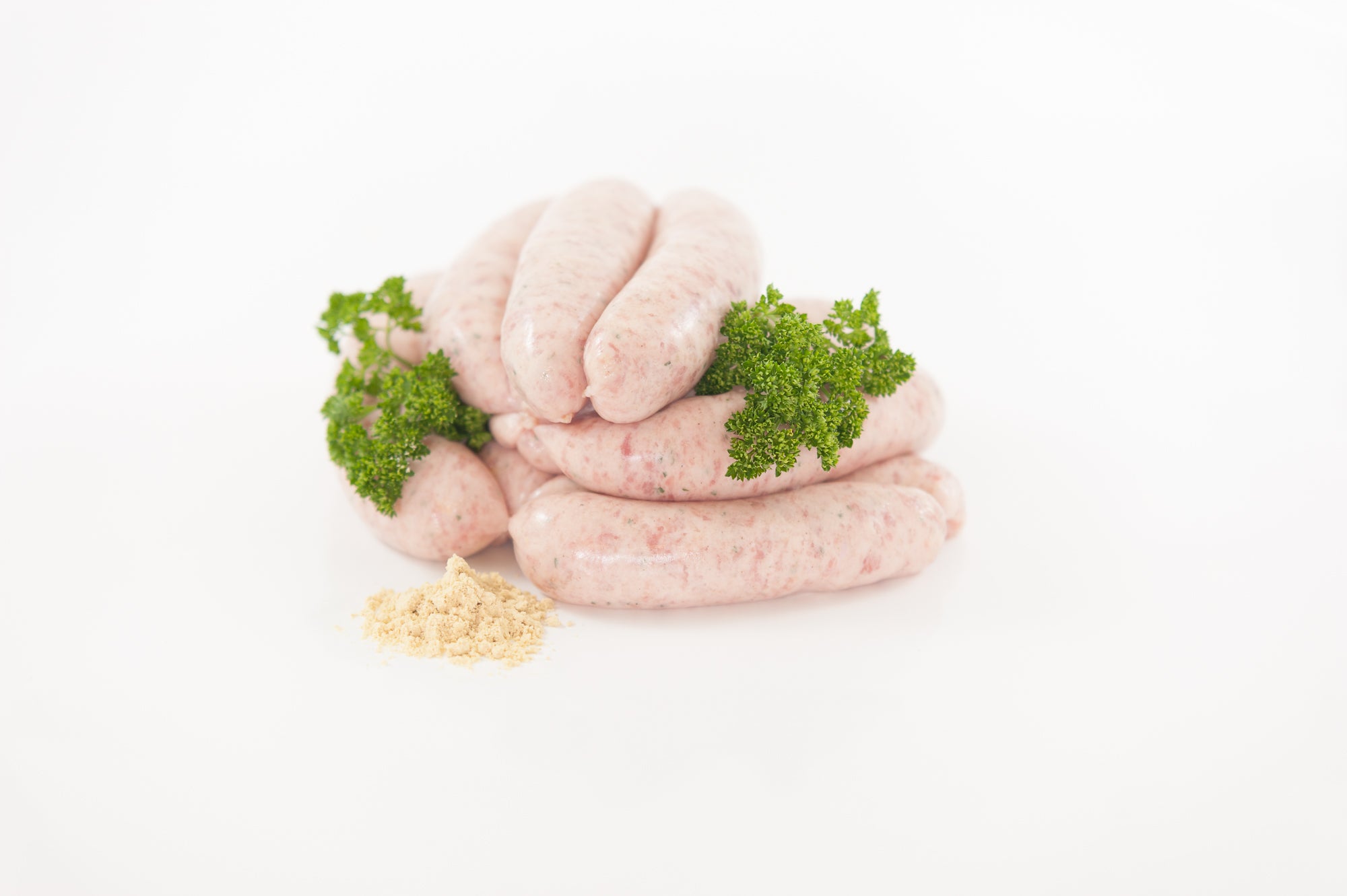 A pack of raw Herterich Bratwurst sausages on a white background, accompanied by parsley leaves and a piece of bread.
