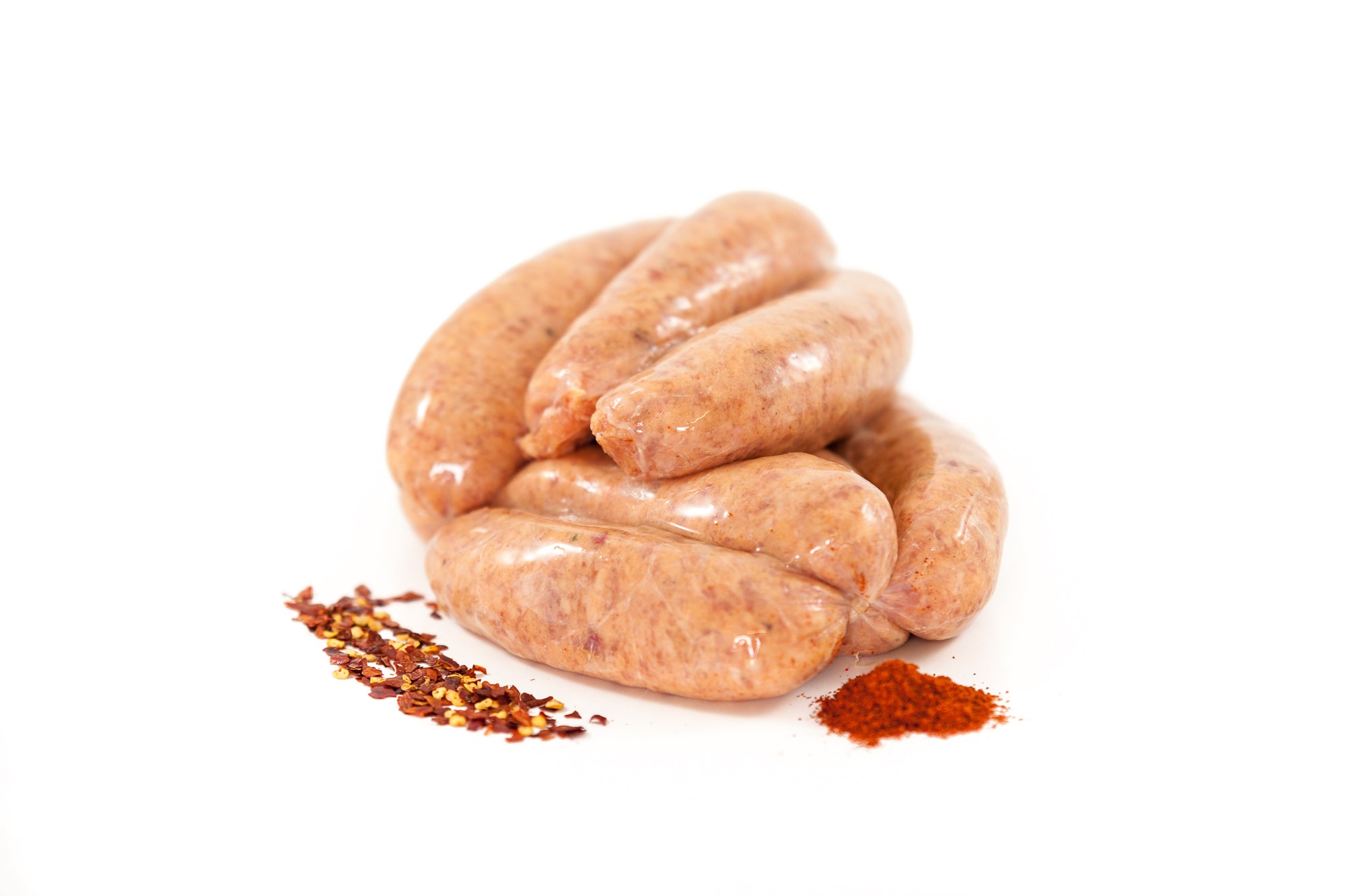 Raw Pork Sausages with Chilli Flakes (350g pack), handlinked and made with 90% Irish pork alongside spices on white background