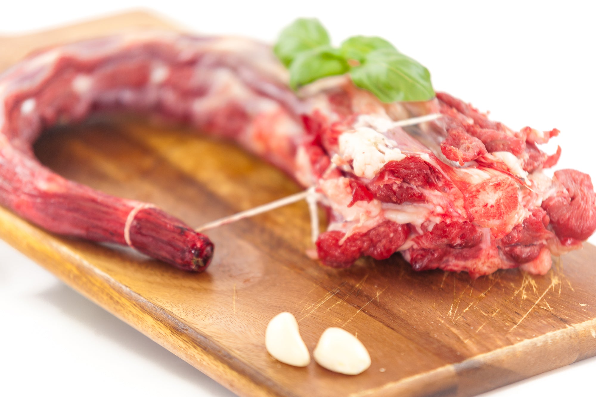 A fresh beef ox-tail on a wooden cutting board with garnish and garlic cloves.