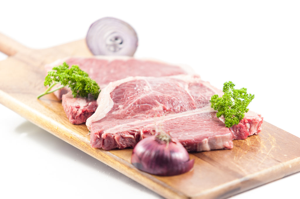 Two raw Dry-Aged T-Bone Steaks from Irish farmed beef, aged for 28+ days, handcut by butchers on a wooden platter 